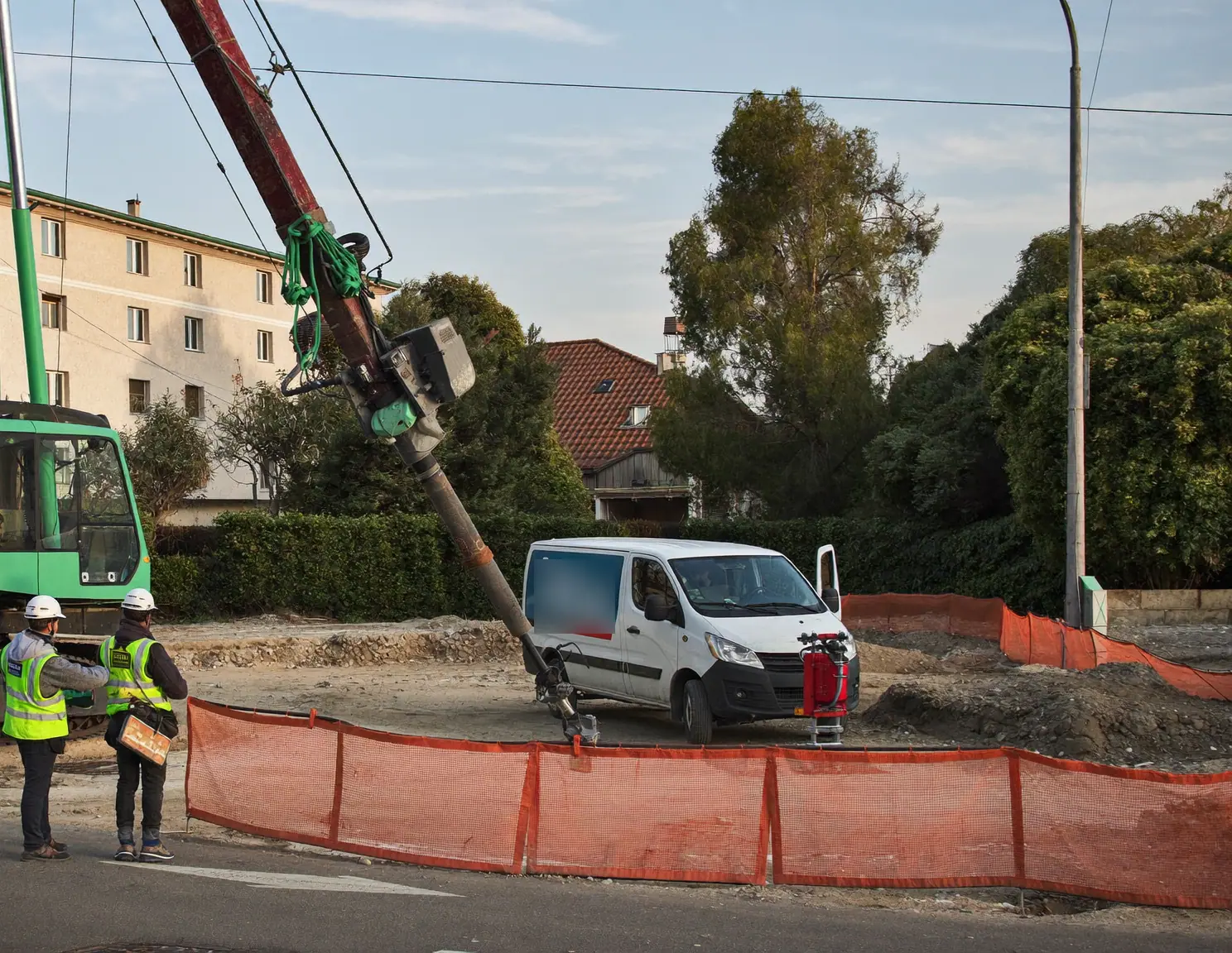 Cantiere stradale con mezzo di perforazione, furgone e operai in giubbotto ad alta visibilità.
